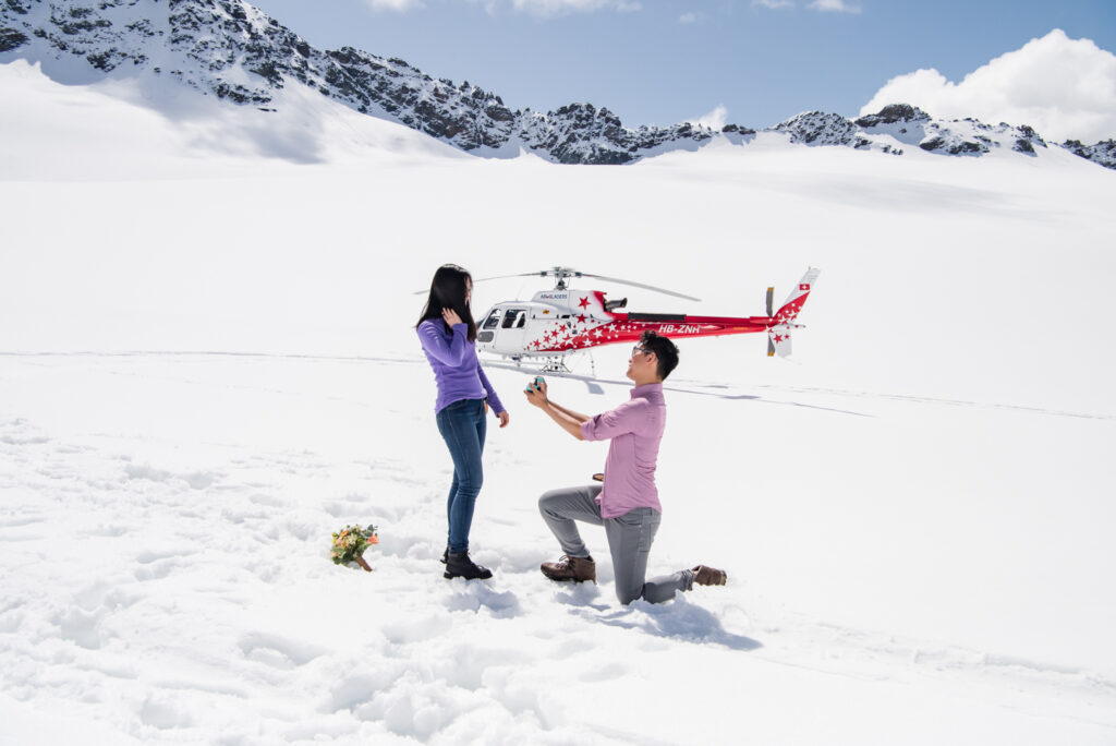 Couple proposing on a glacier in Switzerland with helicopter in the background, luxury adventure proposal