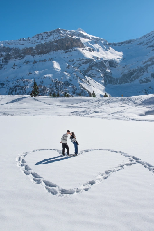 Couple kissing in the snow in a big heart created with their footsteps during an bespoke adventure photo session in switzerland