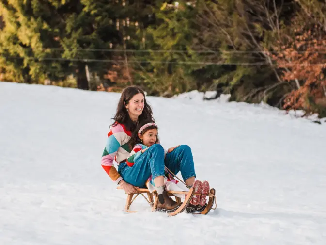 Mother and daughter laughing on a sledge during a winter family portrait session near Montreux