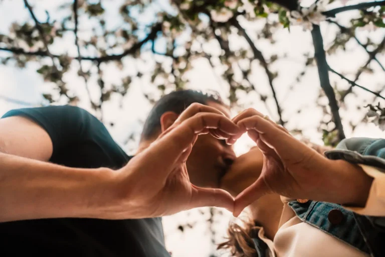 couple holding hands in heart shape while kissing