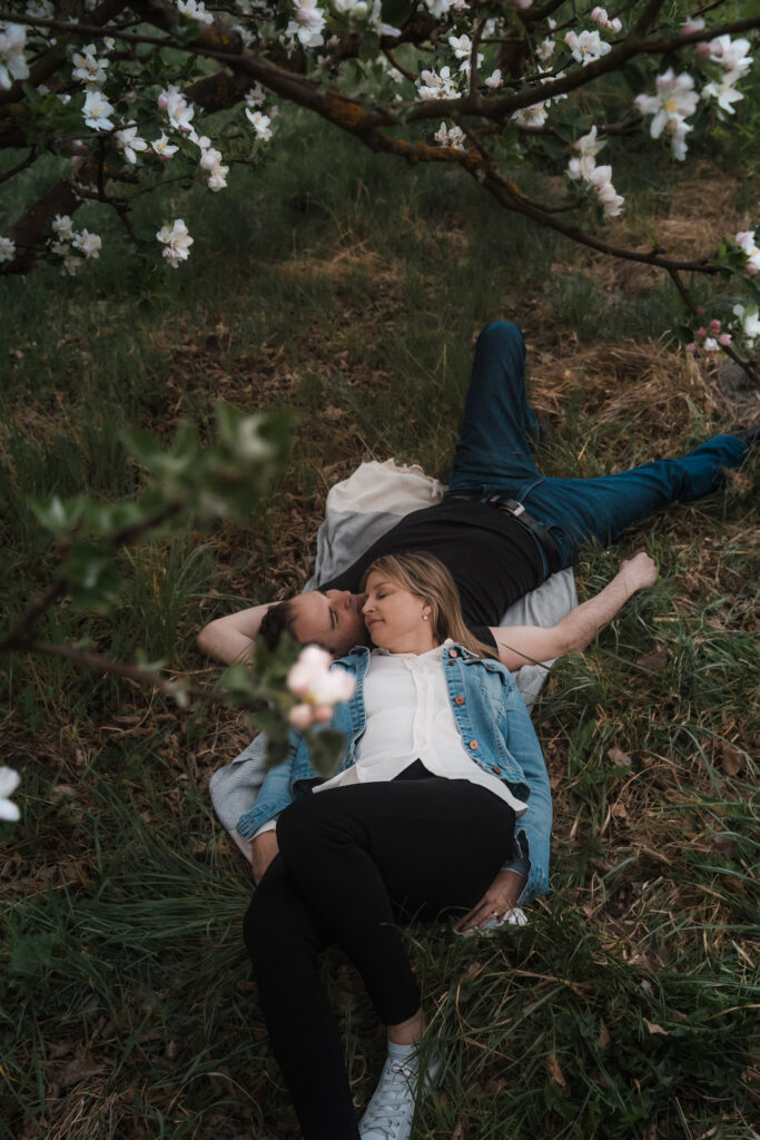 Couple laying on a blanket together among blooming apple trees during a spring anniversary photo session in Switzerland.