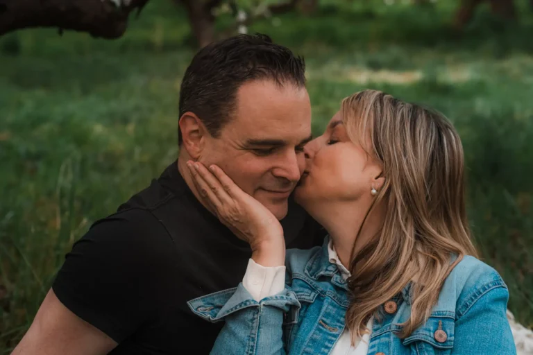 wife kissing husband on cheak during a romantic portrait session outdoors