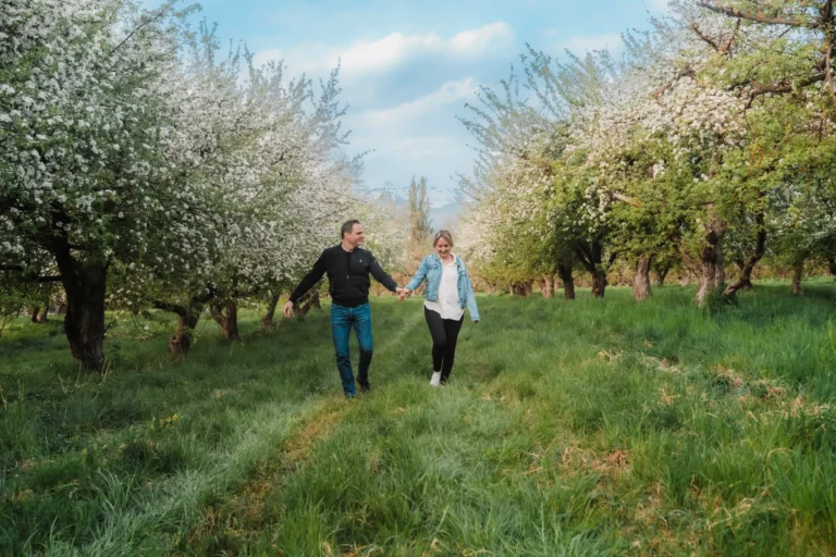 couple walking in blooming apple orchards in wallis, switzerland during an anniversary portrait session with maaike jansen